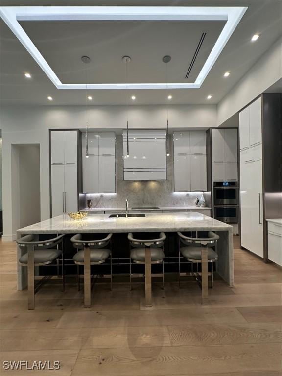 kitchen with a kitchen breakfast bar, backsplash, a large island with sink, hardwood / wood-style flooring, and white cabinets