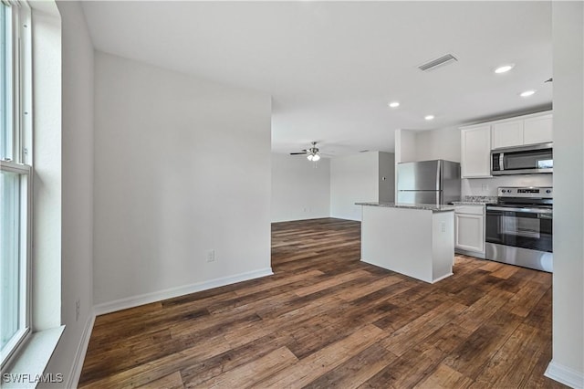 kitchen with appliances with stainless steel finishes, dark hardwood / wood-style flooring, white cabinetry, and a kitchen island