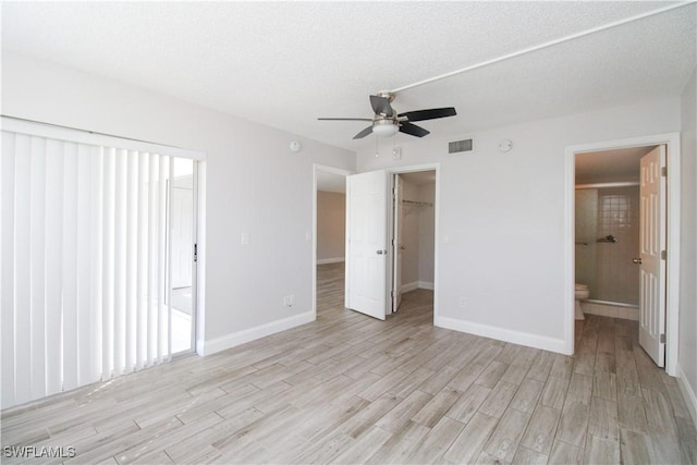 unfurnished bedroom with a spacious closet, ensuite bath, a closet, light wood-type flooring, and ceiling fan