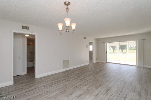 empty room with a notable chandelier, light wood-type flooring, and a textured ceiling