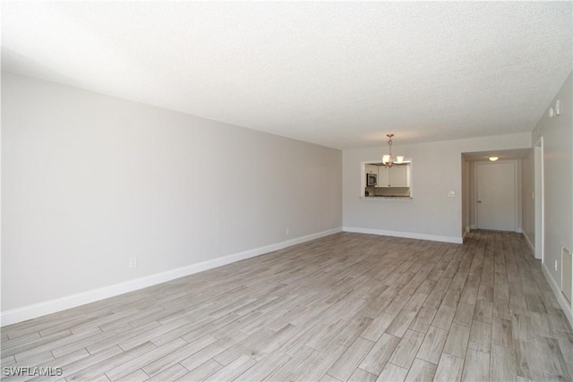 empty room featuring light hardwood / wood-style floors, a textured ceiling, and an inviting chandelier