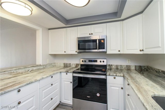 kitchen featuring light stone countertops, white cabinetry, appliances with stainless steel finishes, and a raised ceiling