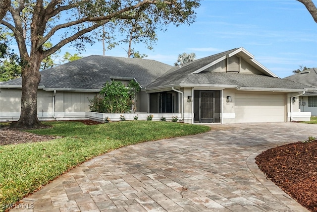 view of front of home featuring a front yard, an attached garage, stucco siding, a shingled roof, and decorative driveway