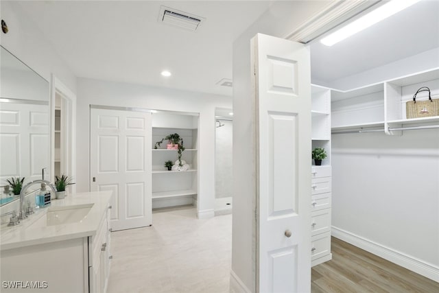 walk in closet with a sink, visible vents, and light wood-style floors