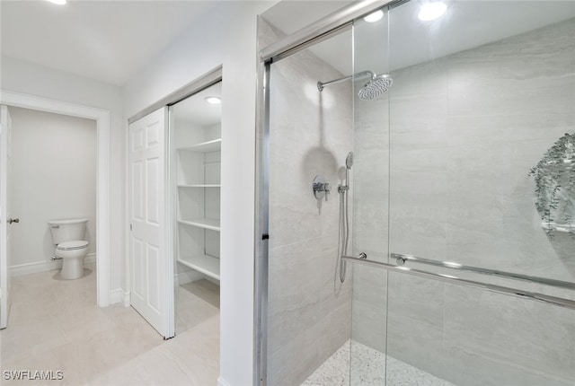 bathroom featuring toilet, baseboards, a stall shower, and a closet