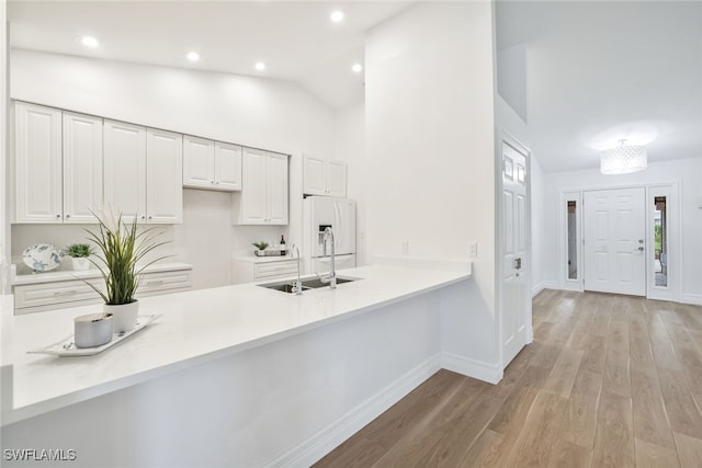 kitchen featuring a peninsula, a sink, light countertops, white fridge with ice dispenser, and light wood-type flooring