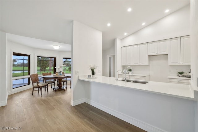 kitchen featuring a sink, wood finished floors, a peninsula, light countertops, and lofted ceiling