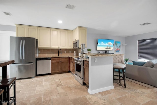 kitchen featuring a kitchen breakfast bar, sink, light stone countertops, kitchen peninsula, and stainless steel appliances