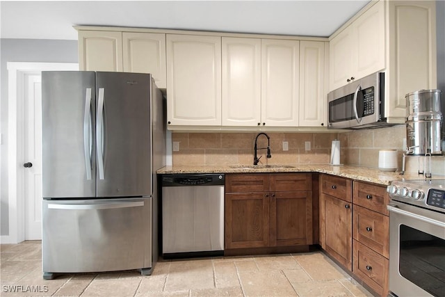 kitchen featuring appliances with stainless steel finishes, tasteful backsplash, light stone counters, sink, and cream cabinets