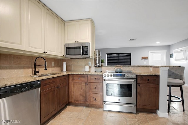 kitchen with light stone counters, a kitchen bar, sink, and appliances with stainless steel finishes