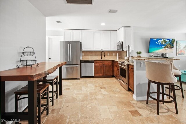 106 Pago Pago Dr W, Naples, FL 34113 - kitchen featuring appliances with stainless steel finishes, stone tile flooring, light stone countertops, backsplash, and white cabinetry