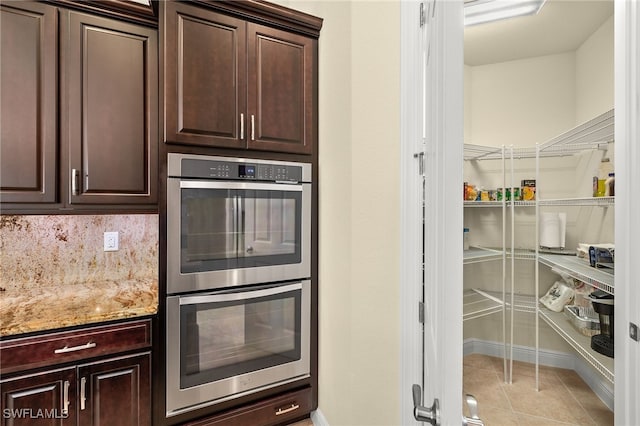 kitchen featuring light stone counters, dark brown cabinetry, and double oven