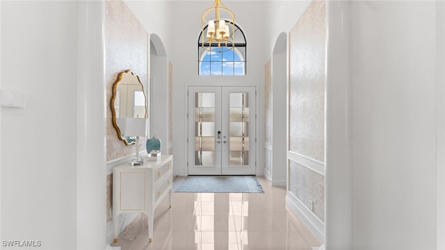 entrance foyer featuring french doors, a towering ceiling, light tile patterned floors, and a notable chandelier