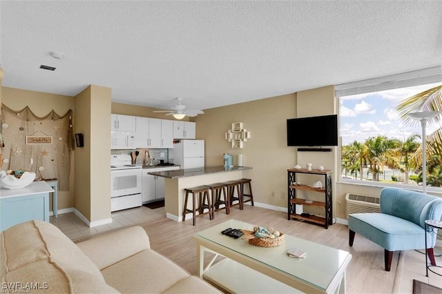 living room with ceiling fan, light hardwood / wood-style floors, a textured ceiling, and a wall mounted AC