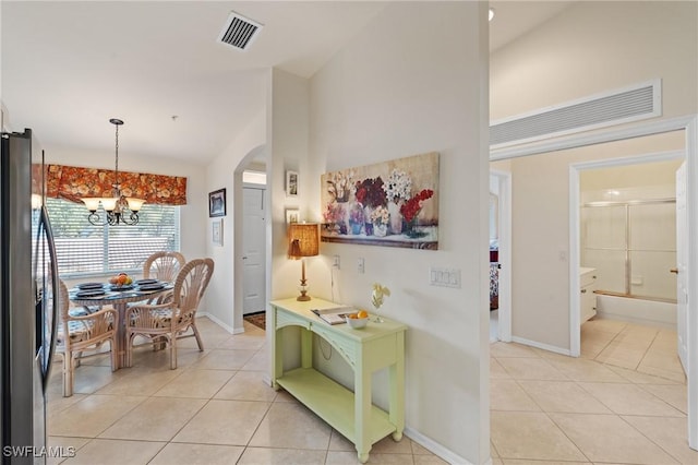 hall featuring a notable chandelier, lofted ceiling, and light tile patterned floors