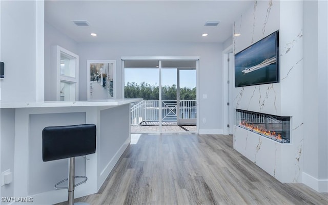 interior space featuring a breakfast bar, a high end fireplace, kitchen peninsula, light wood-type flooring, and white cabinetry