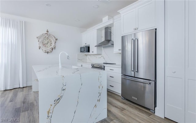 kitchen featuring white cabinets, a kitchen island with sink, wall chimney exhaust hood, and stainless steel appliances