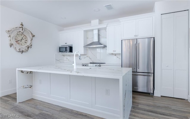 kitchen featuring stainless steel appliances, a kitchen island with sink, wall chimney range hood, wood-type flooring, and white cabinetry