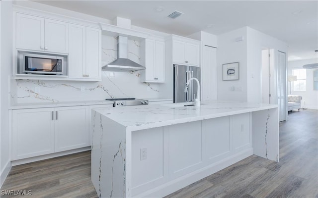 kitchen featuring white cabinetry, a kitchen island with sink, wall chimney exhaust hood, and stainless steel appliances