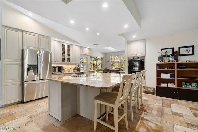 kitchen with light stone counters, vaulted ceiling, white cabinets, stainless steel fridge with ice dispenser, and a kitchen island