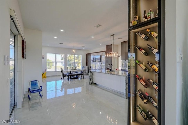 kitchen with light stone countertops, sink, oven, white cabinetry, and hanging light fixtures