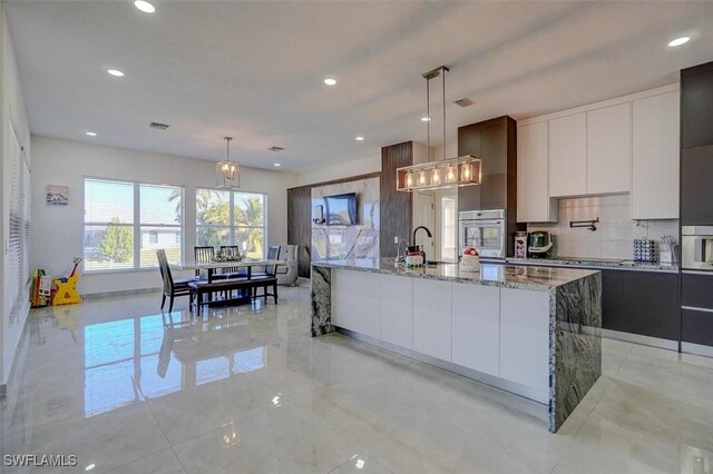 kitchen with white cabinets, hanging light fixtures, and an island with sink