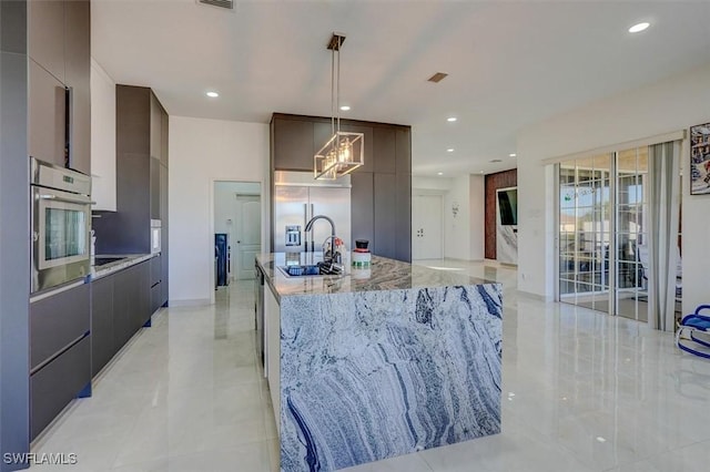 kitchen with a kitchen island with sink, sink, appliances with stainless steel finishes, decorative light fixtures, and light stone counters