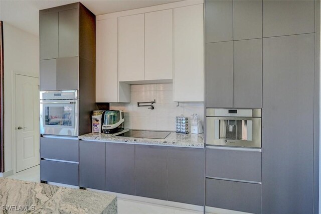 kitchen featuring gray cabinets, black electric cooktop, oven, and light stone counters