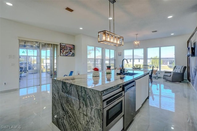 kitchen featuring sink, stainless steel appliances, light stone counters, an island with sink, and decorative light fixtures