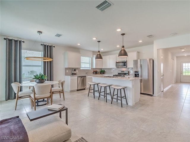 kitchen featuring stainless steel appliances, a center island, white cabinets, decorative light fixtures, and backsplash