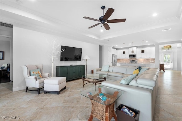 tiled living room with a tray ceiling, ceiling fan, and ornamental molding