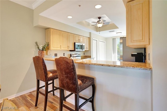 kitchen featuring a breakfast bar area, ceiling fan, kitchen peninsula, stainless steel appliances, and light stone countertops