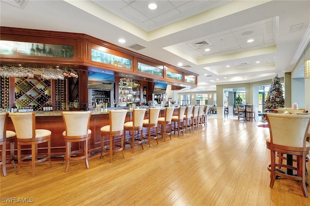 bar featuring a tray ceiling and light hardwood / wood-style flooring