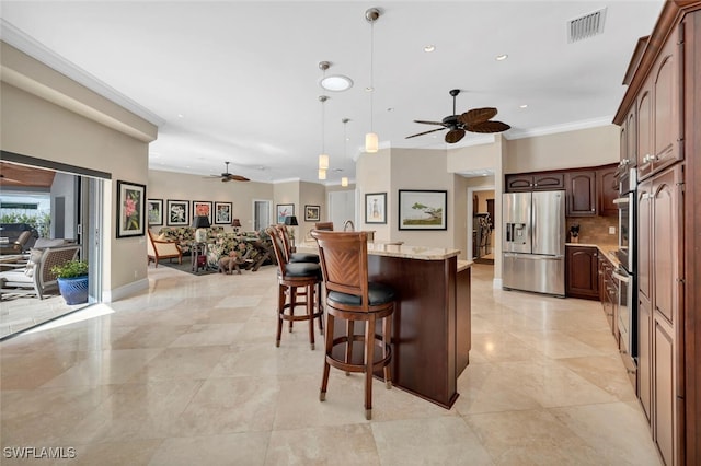 kitchen featuring appliances with stainless steel finishes, ornamental molding, a kitchen island, hanging light fixtures, and a breakfast bar area