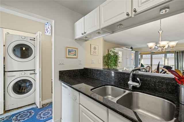 kitchen featuring dishwasher, sink, stacked washer / dryer, dark stone counters, and white cabinets