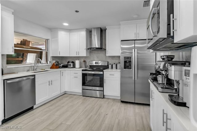 kitchen with white cabinets, light hardwood / wood-style floors, wall chimney range hood, and appliances with stainless steel finishes