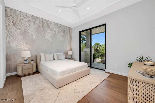bedroom featuring an accent wall, wood finished floors, a raised ceiling, baseboards, and access to outside