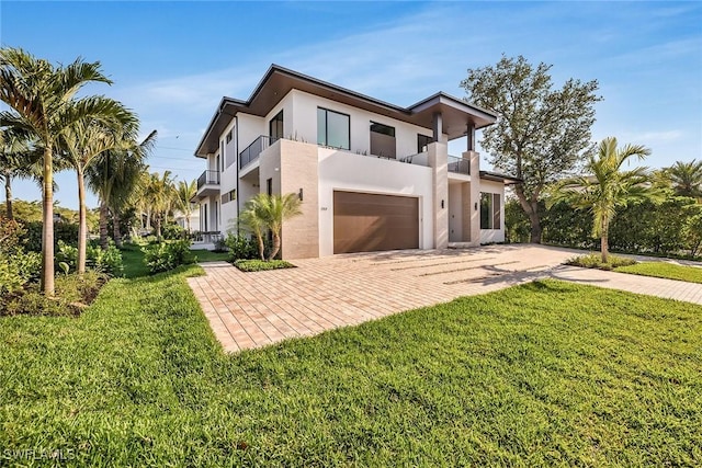 contemporary house with a balcony, stucco siding, an attached garage, decorative driveway, and a front yard