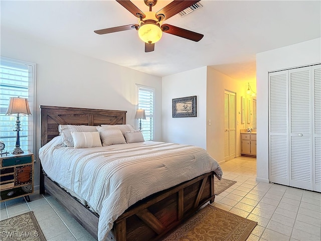 tiled bedroom with ensuite bath, ceiling fan, and two closets