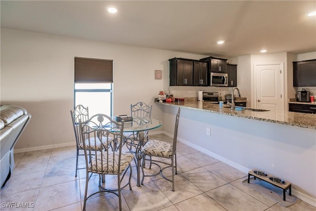 kitchen featuring sink, appliances with stainless steel finishes, light tile patterned flooring, light stone counters, and kitchen peninsula