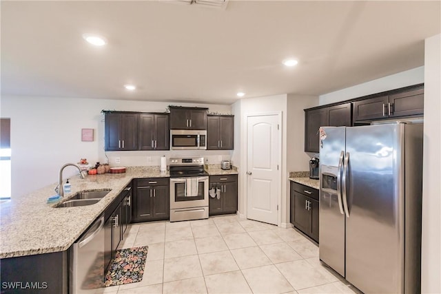 kitchen featuring kitchen peninsula, light stone countertops, dark brown cabinets, stainless steel appliances, and sink