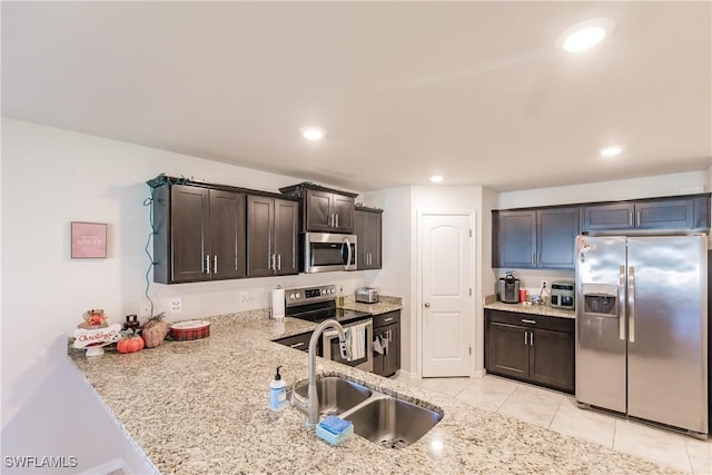 kitchen with sink, appliances with stainless steel finishes, light tile patterned flooring, light stone counters, and dark brown cabinetry