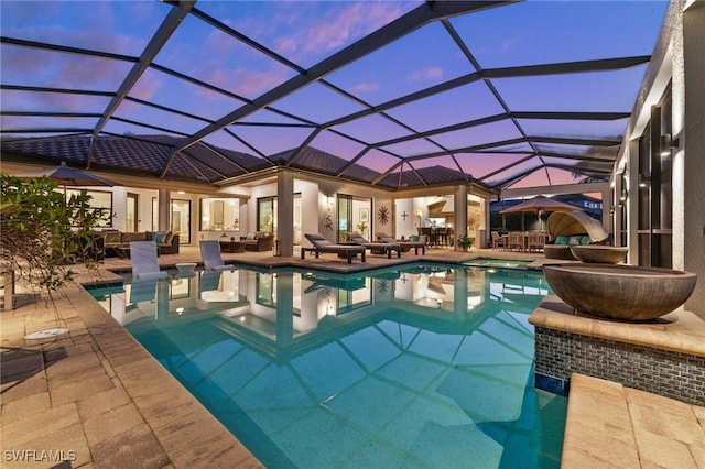 pool at dusk with glass enclosure and a patio area