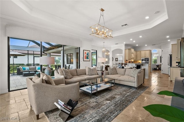 living room with an inviting chandelier, crown molding, and a tray ceiling