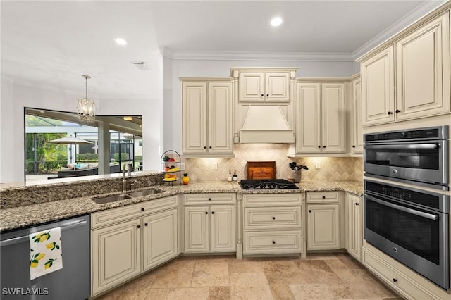 kitchen with custom exhaust hood, sink, appliances with stainless steel finishes, cream cabinetry, and decorative light fixtures