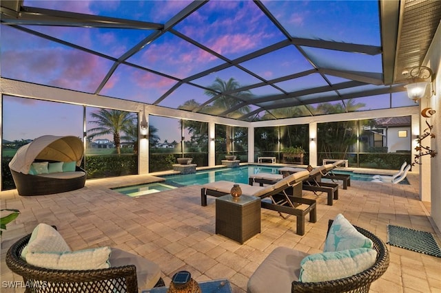 pool at dusk featuring glass enclosure, an in ground hot tub, and a patio area