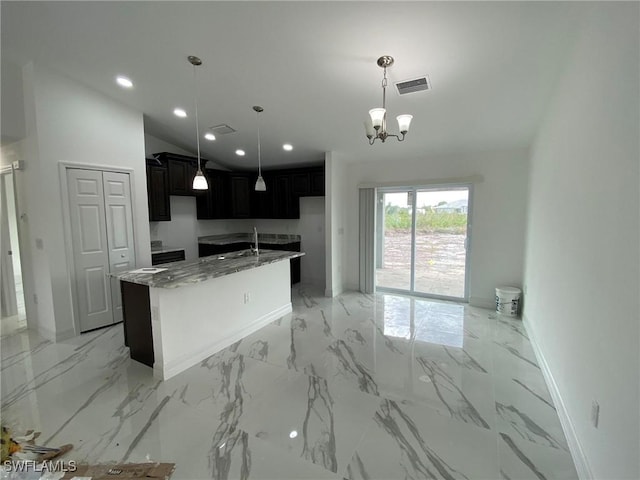 kitchen featuring pendant lighting, a center island with sink, sink, a notable chandelier, and light stone counters