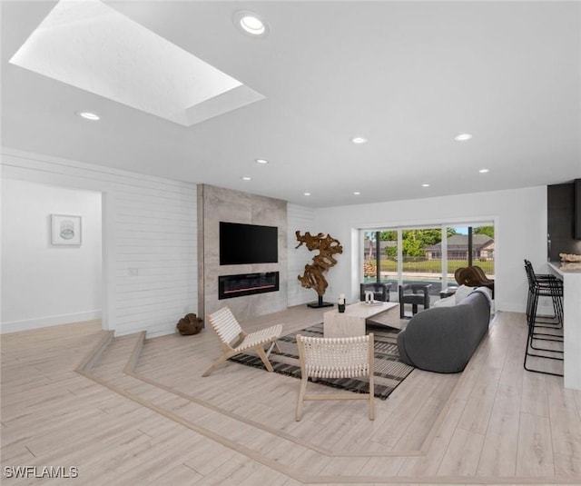 living room featuring light wood-type flooring, a high end fireplace, and a skylight