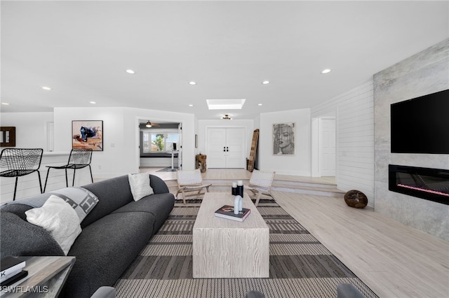 living room featuring a tiled fireplace, ceiling fan, and wood-type flooring