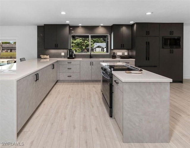 kitchen featuring stainless steel microwave, sink, black electric range, light hardwood / wood-style flooring, and kitchen peninsula